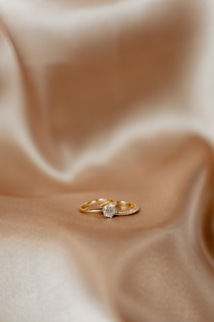 A pair of gold rings resting on a smooth, silky fabric. One of the rings features a prominent diamond, positioned centrally, adding a touch of elegance.