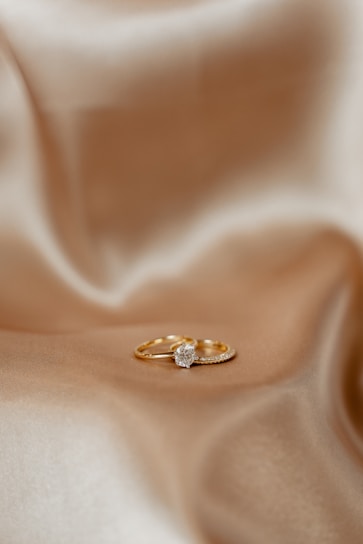 A pair of gold rings resting on a smooth, silky fabric. One of the rings features a prominent diamond, positioned centrally, adding a touch of elegance.