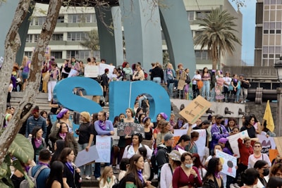 A large group of people, predominantly women, are gathered for a protest or rally. They are holding signs with various messages, many of which focus on women's rights and empowerment. Some participants are wearing purple, a color often associated with feminist movements. The atmosphere is lively and engaged, with a sense of solidarity among the crowd.