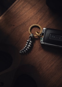 A keychain with a metallic spiral charm rests on a wooden surface alongside a car key. The keychain ring features engraved text, creating a luxurious and sophisticated impression.