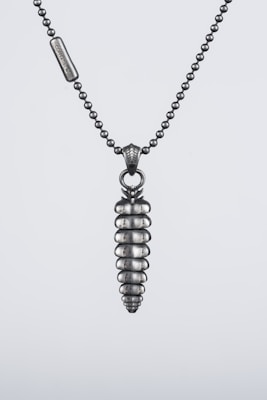 A silver necklace with a chain made of small metallic beads and a pendant shaped like a screw. The pendant features segmented, rounded layers and hangs from a decorative bail. The overall design is sleek and industrial.
