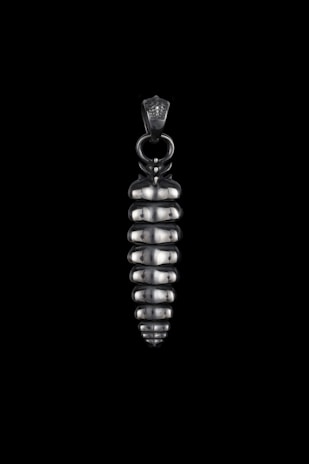 A close-up of a handcrafted silver geometric moth pendant resting on a soft white linen fabric