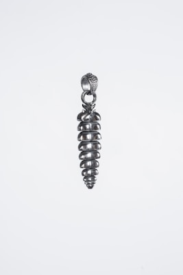A metallic pendant shaped like a screw is suspended against a plain background. The pendant features a spiraled design, showcasing a shiny silver finish with a loop at the top for attachment.