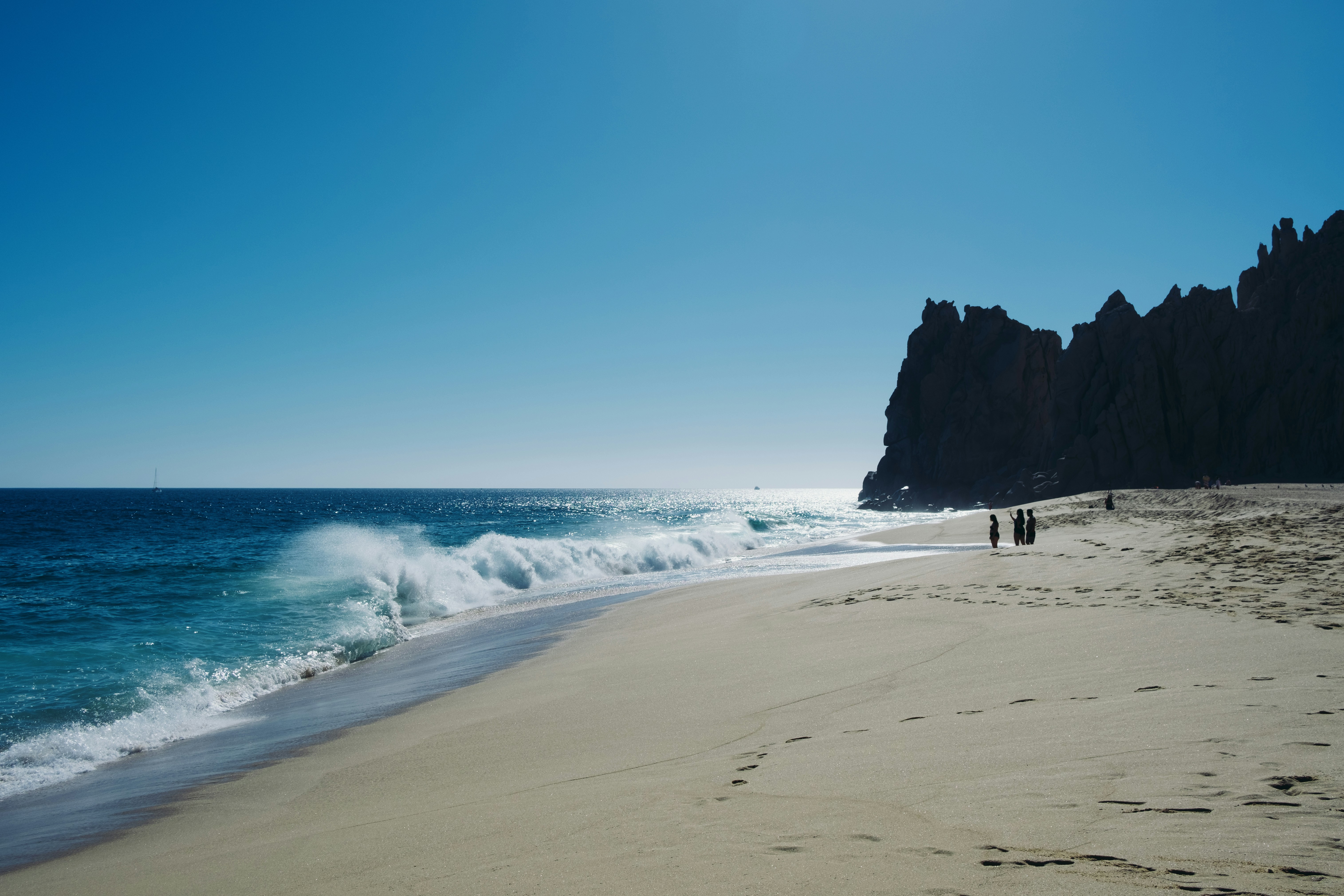 a couple of people walking along a beach next to the ocean, 