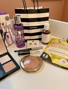 An arrangement of various cosmetic and skincare products displayed, including Clinique makeup remover, an eyeshadow palette, Kiehl's cleanser, vitamin eye mask, a pair of earrings, and several other makeup items. A black and white striped Sephora shopping bag is also present.