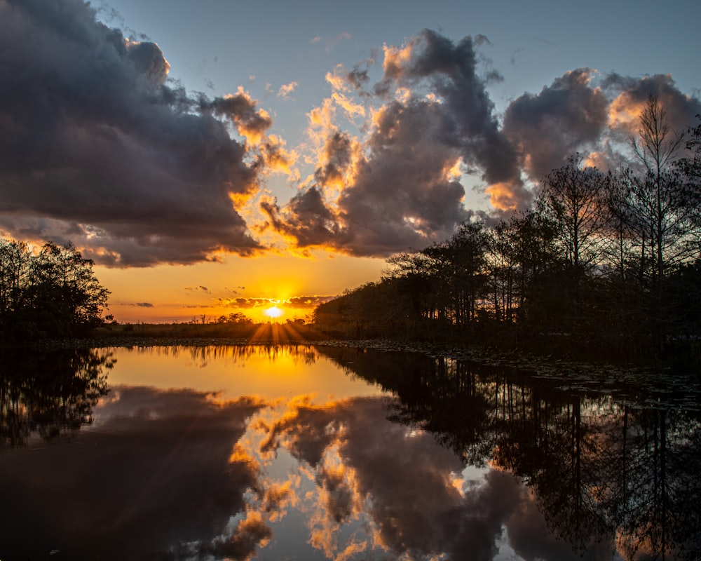 the sun is setting over a lake surrounded by trees