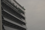 A modern building facade with rows of tilted solar panels mounted along the structure, set against a cloudy sky.