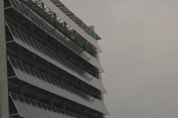 A modern building facade with rows of tilted solar panels mounted along the structure, set against a cloudy sky.