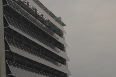 A modern building facade with rows of tilted solar panels mounted along the structure, set against a cloudy sky.