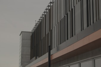 A modern building with vertical metal slats covering the exterior facade, creating a pattern with strong lines. The structure features a combination of concrete and metal materials.