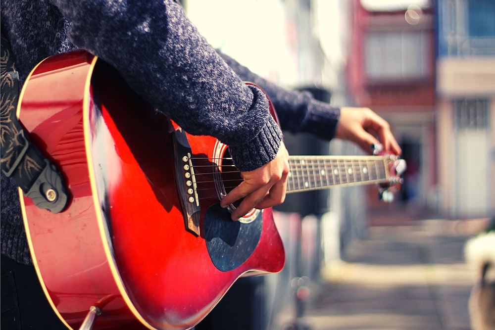 a person playing a red guitar on a city street