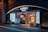 The entrance of a beer hall with neon lighting and signage. Advertisements for German sizzling sausage and beer are prominently displayed. The building has a modern design with decorative lights creating an inviting atmosphere.