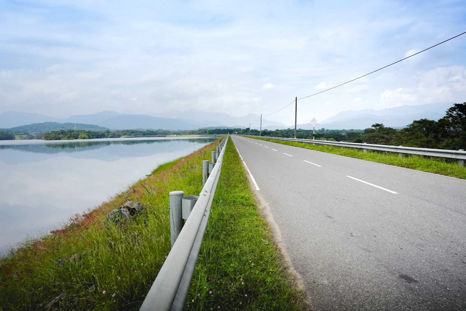A reservoir-side road beneath broad skies in Sri Lanka