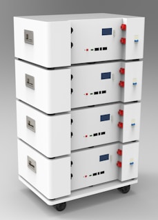 A stack of four white rectangular units with handles and various connectors on the sides. Each unit has a digital display and several ports, knobs, and buttons. The casing is sleek and minimalistic, and the set is mounted on small wheels for mobility, suggesting a modular and portable design.