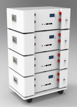 A stack of four white rectangular units with handles and various connectors on the sides. Each unit has a digital display and several ports, knobs, and buttons. The casing is sleek and minimalistic, and the set is mounted on small wheels for mobility, suggesting a modular and portable design.