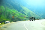 a truck driving down a road next to a lush green hillside