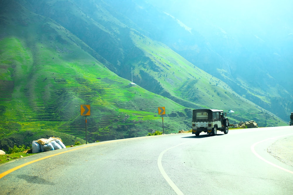 a truck driving down a road next to a lush green hillside