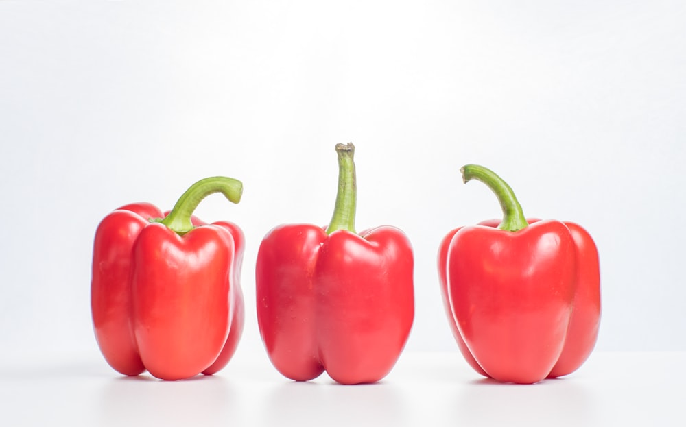 three red peppers with green stems on a white surface