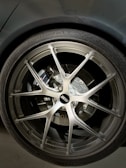 A close-up of a car wheel featuring a BBS alloy rim, with a visible brake disc and caliper behind it. The tire is labeled with 'SportContact 7' by Continental, indicating a high-performance tire. The metallic finish of the rim contrasts with the darker tones of the tire and the car body.