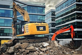 An excavator is placed on top of a pile of rubble amidst a construction site. The construction equipment is positioned in an urban environment, surrounded by modern glass office buildings. The machinery is labeled with the brand 'Caterpillar' and the name 'AWR Abbruch'. A second orange excavator stands nearby, contributing to the ongoing demolition work. The atmosphere suggests a busy site as the excavators appear functional and operational.