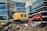 An excavator is placed on top of a pile of rubble amidst a construction site. The construction equipment is positioned in an urban environment, surrounded by modern glass office buildings. The machinery is labeled with the brand 'Caterpillar' and the name 'AWR Abbruch'. A second orange excavator stands nearby, contributing to the ongoing demolition work. The atmosphere suggests a busy site as the excavators appear functional and operational.