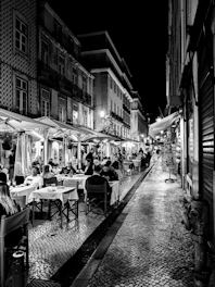A lively street in Toledo with people enjoying tapas at outdoor tables under warm lights.
