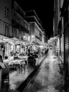 A lively street in Toledo with people enjoying tapas at outdoor tables under warm lights.