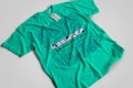 A turquoise t-shirt with an intricate blue graphic design and text on the front. The design includes various abstract shapes, musical elements, and patterns. The text reads 'New Breed of Deep House' with additional words above it that are difficult to discern.