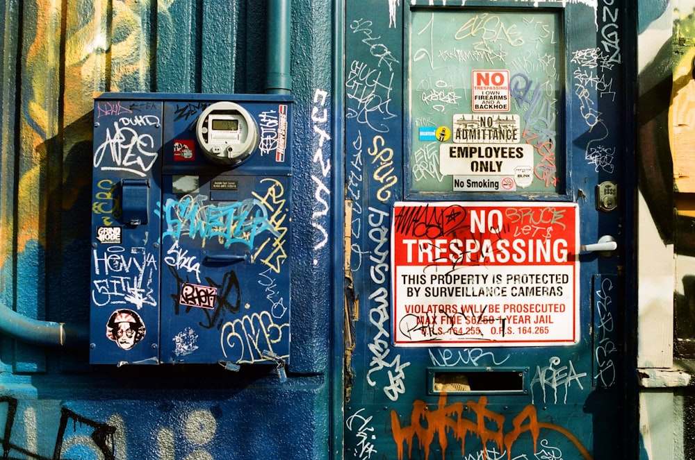 a parking meter covered in graffiti next to a no trespassing sign