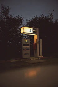 A single, illuminated vintage gas pump stands in a dark, secluded area surrounded by dense foliage. The pump is marked with the number 5 and labeled for diesel fuel.