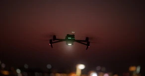 A dynamic FPV drone flying through an urban nightscape illuminated by electric blue lights.