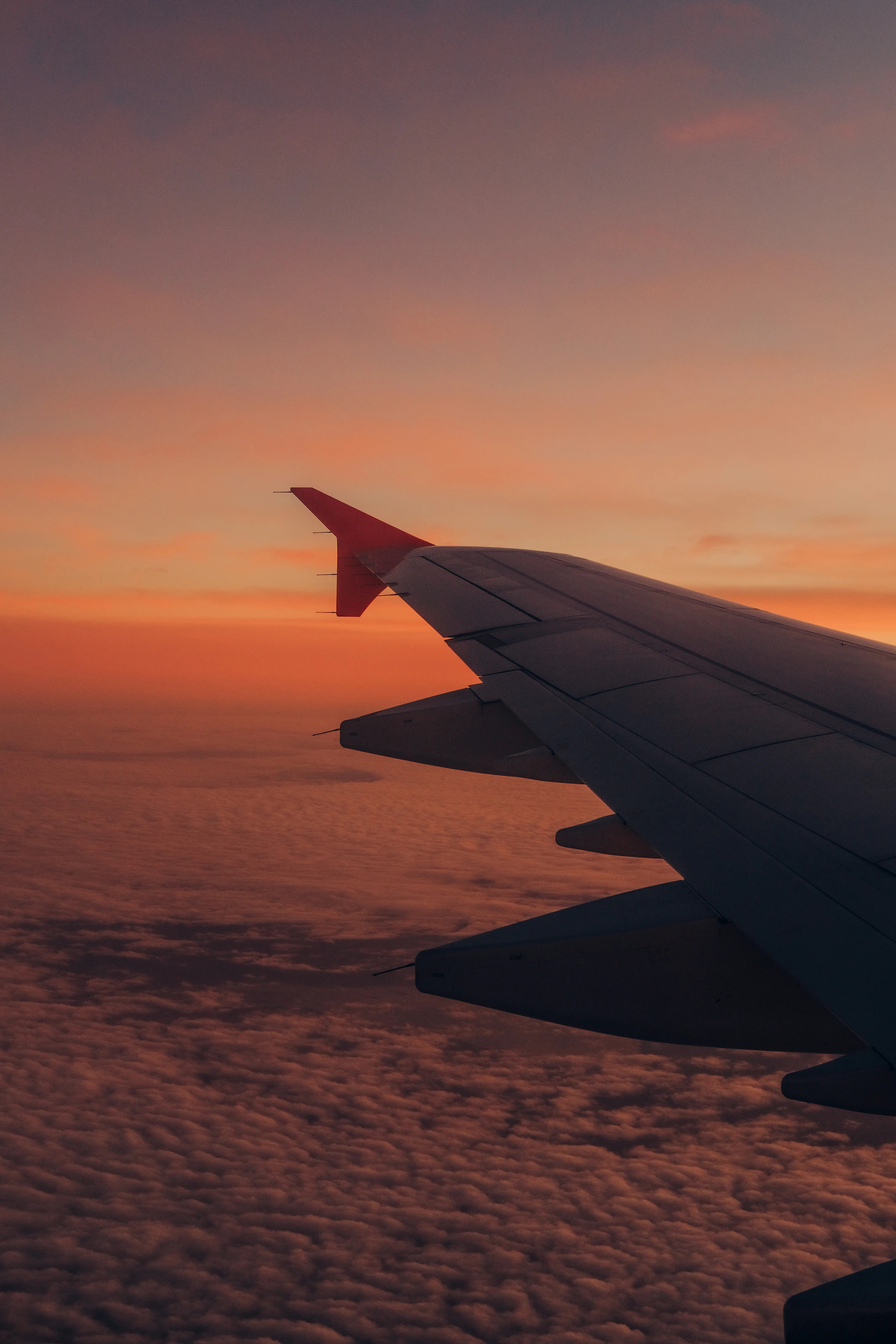 Airplane wing above the clouds at sunset