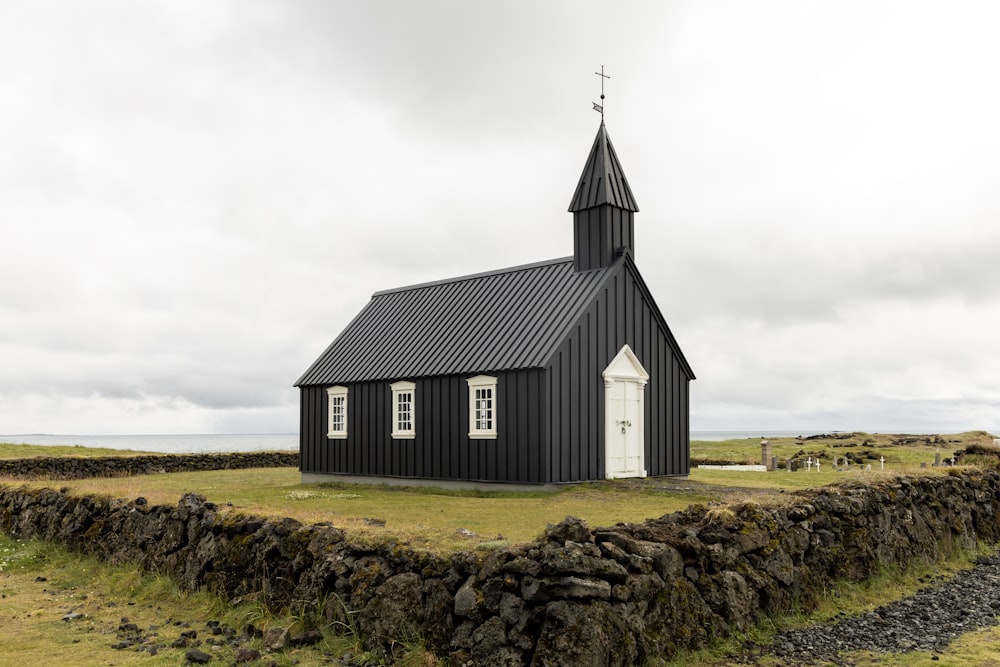 a small black church with a steeple on a grassy field