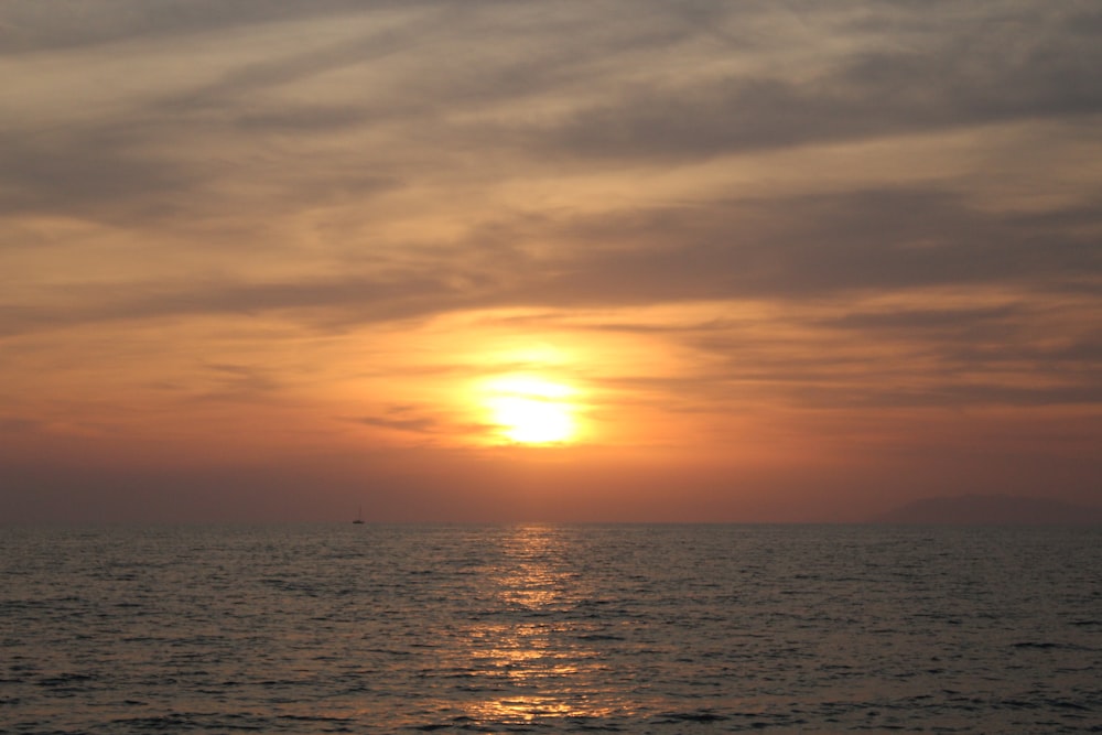 the sun is setting over the ocean on a cloudy day