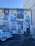 The wall is covered with vibrant murals depicting Cuban flags, tropical scenes, figures playing music, and a mix of artistic symbols and text. A classic blue and white car is parked in front of the colorful building.