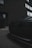 A close-up of a car's front grille with a sleek, modern design, including a distinctive logo. The setting is urban, with a brick exterior of a building and large windows in the background. The overall ambiance is moody with low lighting.