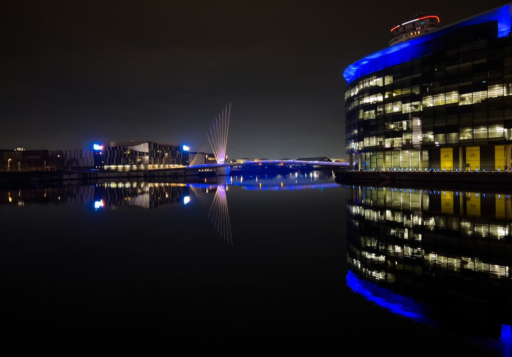 a building is lit up at night next to a body of water