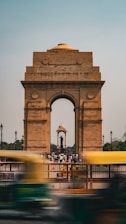 a yellow bus driving past a large stone arch