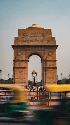 a yellow bus driving past a large stone arch