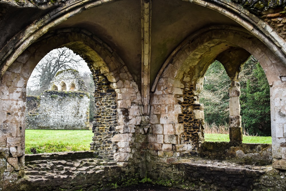 an old stone building with arches and a grassy field in the background