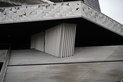 An abstract architectural structure composed of angular and linear elements. The design features repeating geometric patterns with a combination of smooth and textured surfaces in neutral tones.