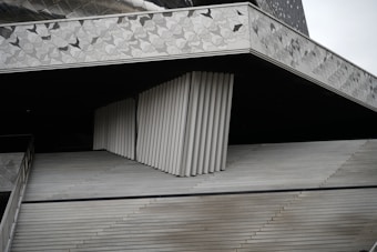 An abstract architectural structure composed of angular and linear elements. The design features repeating geometric patterns with a combination of smooth and textured surfaces in neutral tones.
