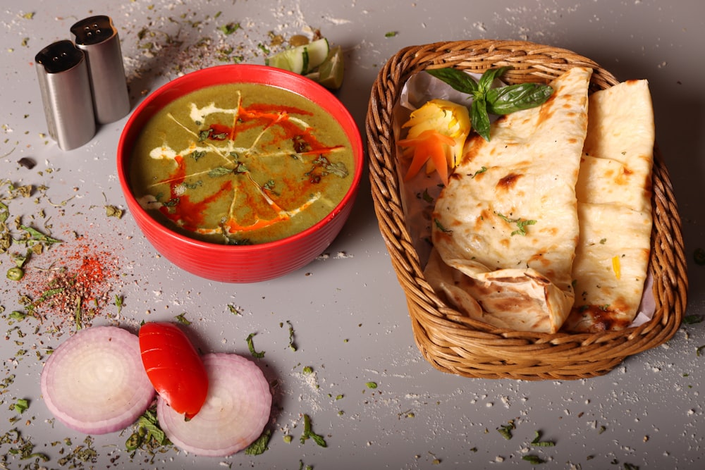 a bowl of soup next to a basket of pita bread