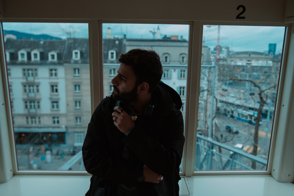 a man standing in front of a window looking out at a city