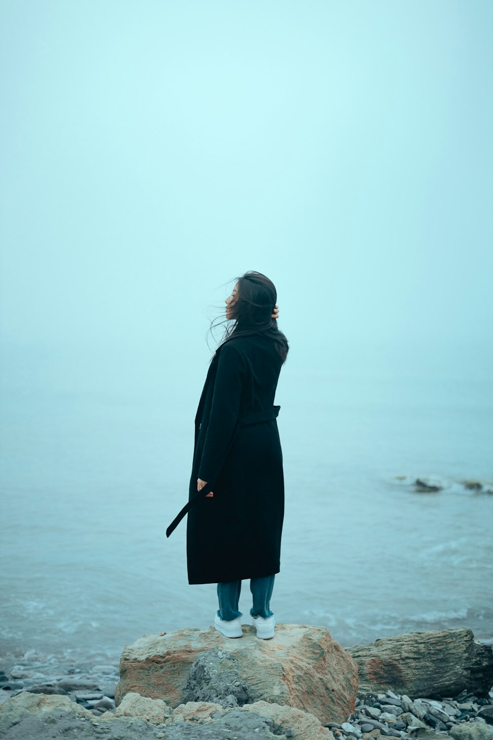 a woman standing on a rock looking out at the ocean