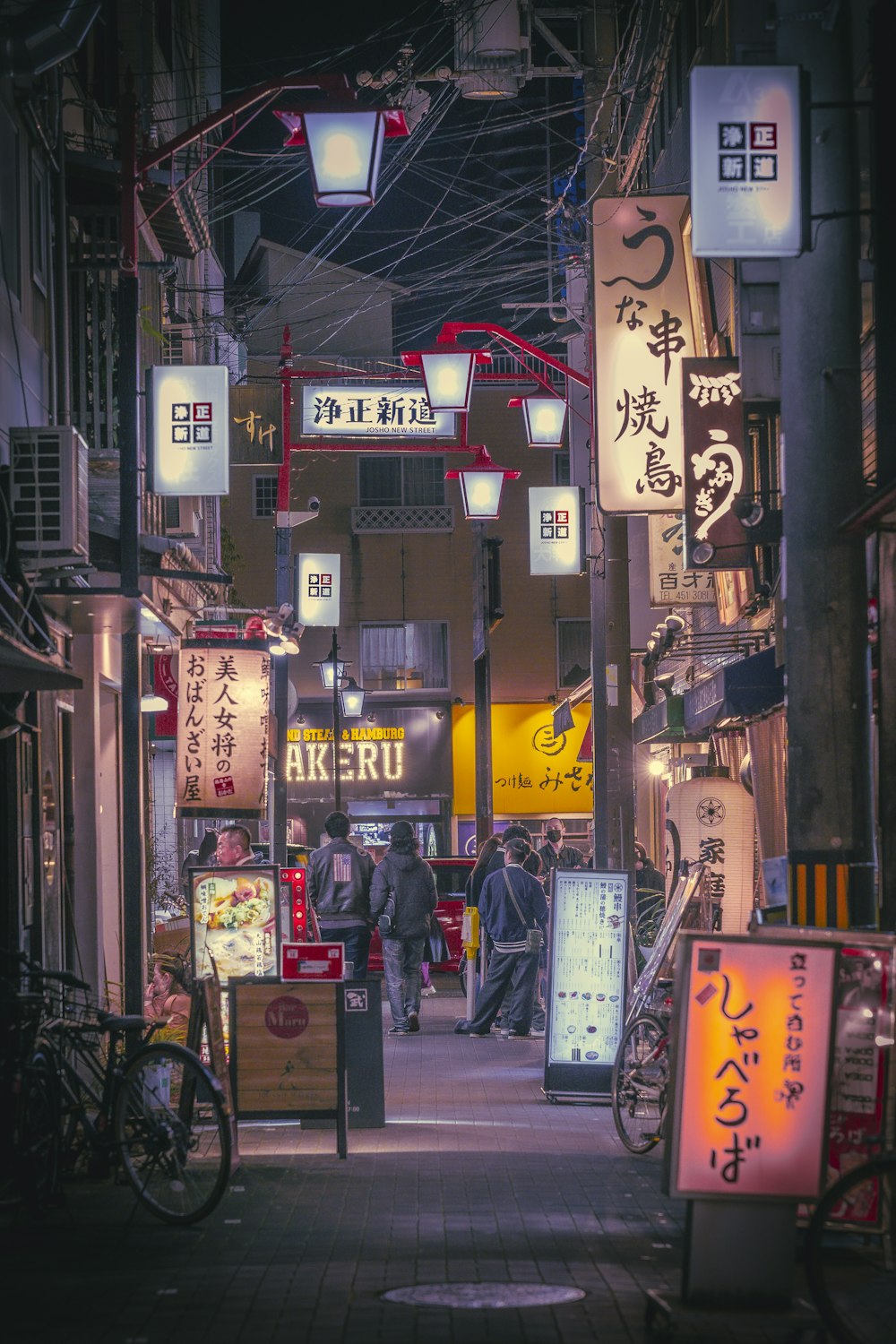 a narrow city street at night with people walking