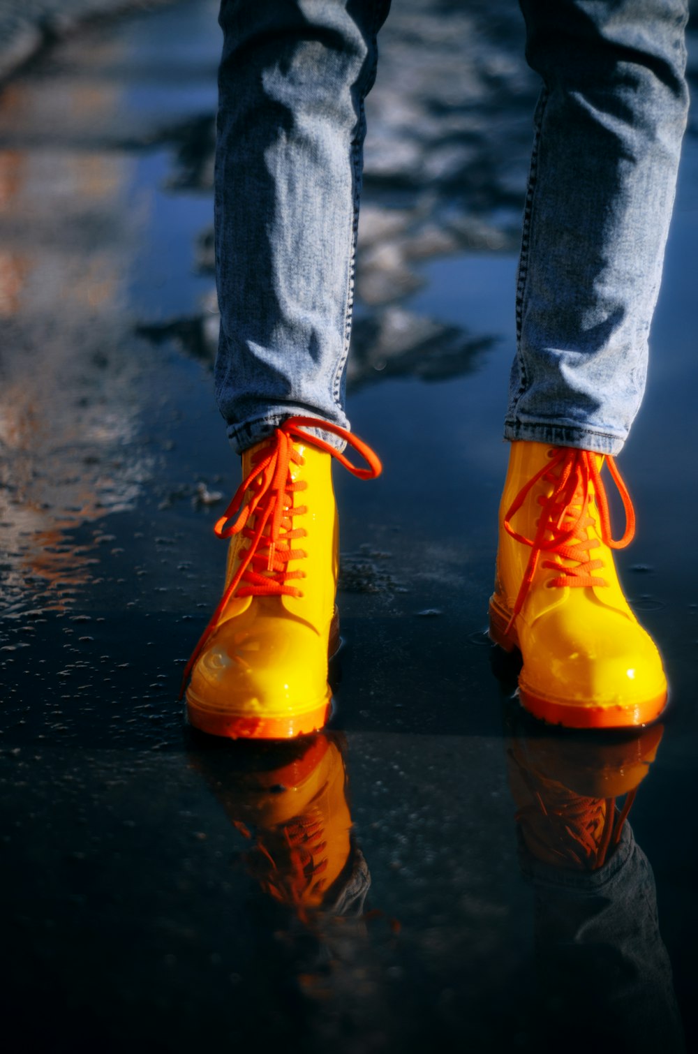 uma pessoa vestindo botas amarelas em pé em uma superfície molhada