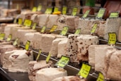 A display of various blocks of halva, featuring different colors and textures, with yellow price tags. The halva blocks are arranged neatly in rows, showcasing different types and flavors.