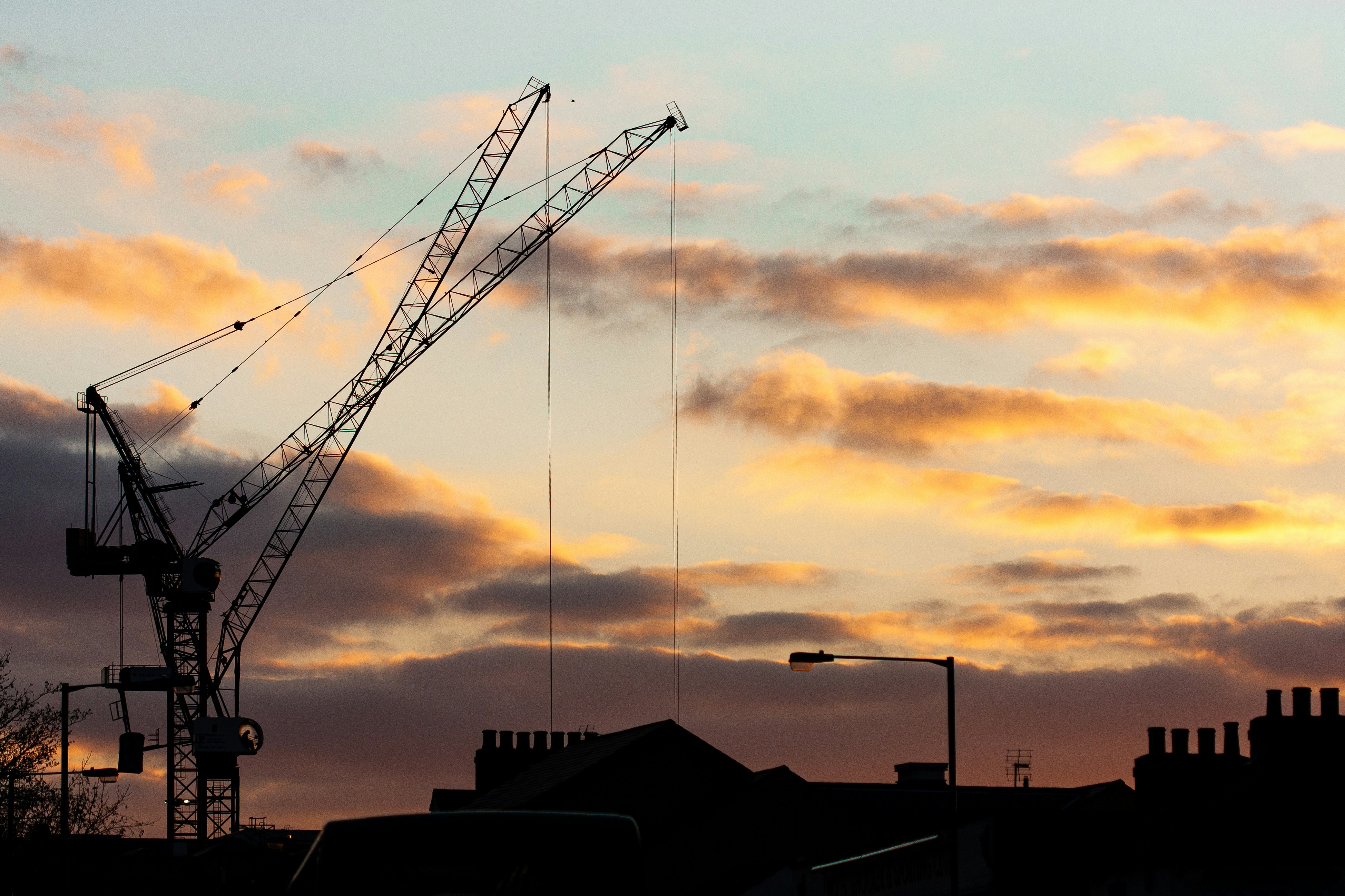 The silhouette of construction cranes against rooftops at sunset