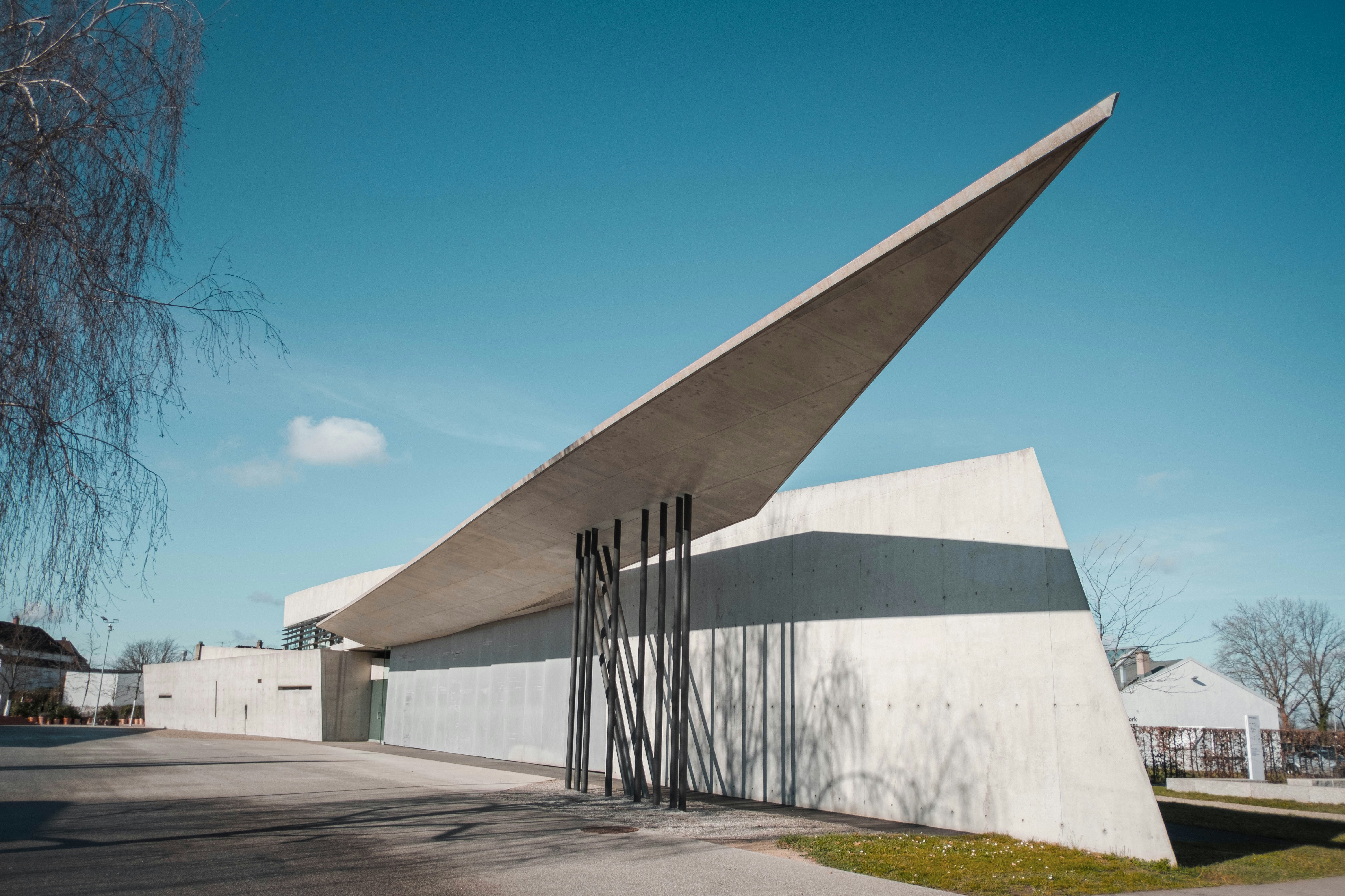 A building with a large triangular roof next to a tree photo – Free ...